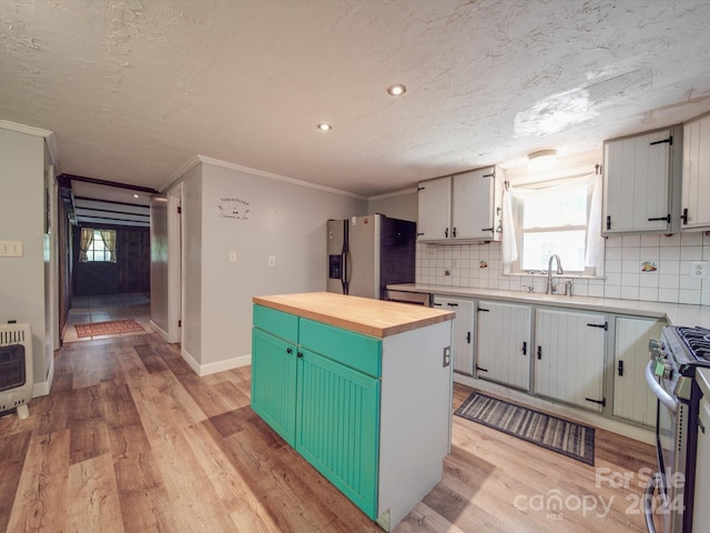 kitchen featuring a kitchen island, butcher block countertops, heating unit, light wood-type flooring, and appliances with stainless steel finishes