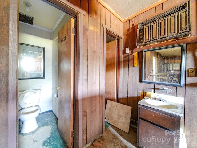 bathroom with toilet, crown molding, wood walls, and vanity