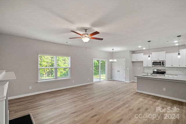 kitchen featuring appliances with stainless steel finishes, light wood-type flooring, light stone counters, decorative light fixtures, and white cabinetry