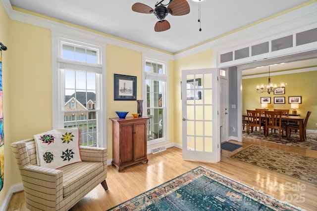 sitting room featuring visible vents, crown molding, baseboards, wood finished floors, and ceiling fan with notable chandelier