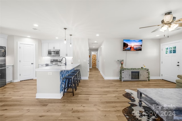 kitchen with white cabinetry, a breakfast bar area, stainless steel appliances, decorative light fixtures, and sink