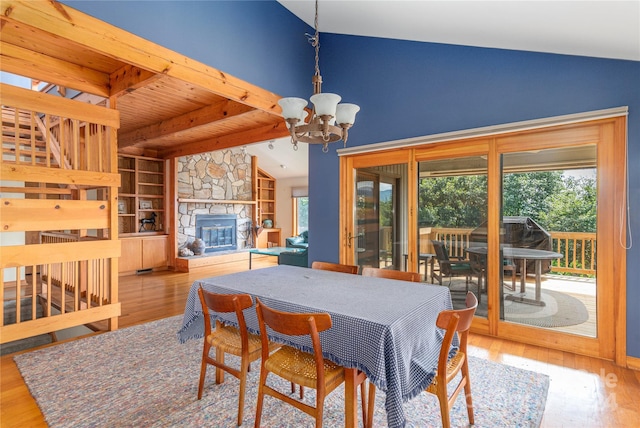 dining area with vaulted ceiling with beams, light wood-style flooring, an inviting chandelier, wood ceiling, and a stone fireplace