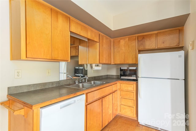 kitchen featuring light wood-style flooring, white appliances, a sink, brown cabinets, and dark countertops