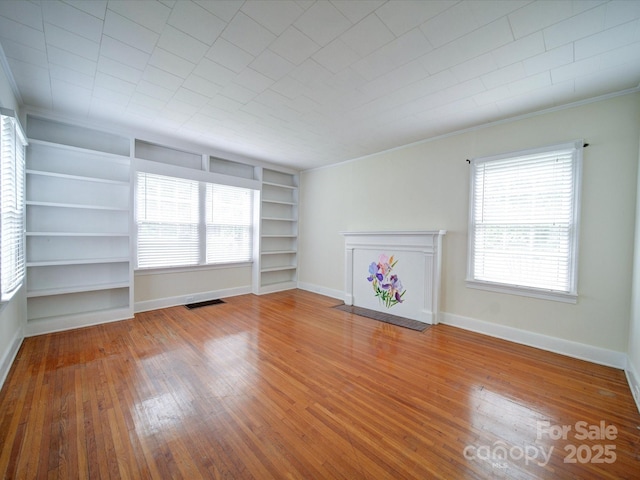 unfurnished living room with built in shelves, hardwood / wood-style flooring, and a wealth of natural light