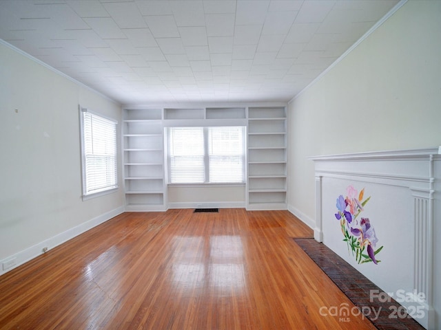 unfurnished living room with built in shelves, crown molding, and light hardwood / wood-style flooring