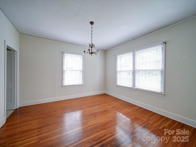 empty room featuring a wealth of natural light, a chandelier, and wood-type flooring