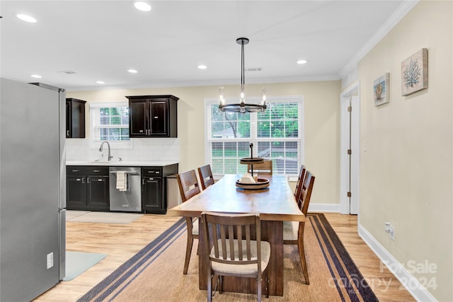 dining area featuring sink, an inviting chandelier, ornamental molding, and light hardwood / wood-style floors