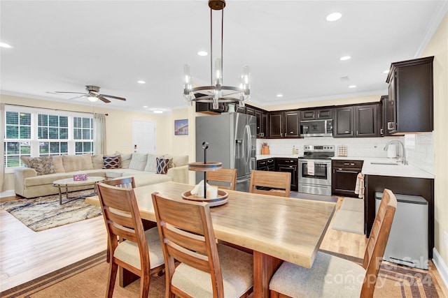 dining space with light wood-type flooring, ornamental molding, ceiling fan with notable chandelier, and sink