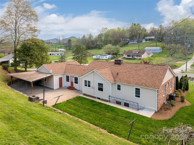 rear view of property featuring a mountain view, central AC, a patio area, and a lawn