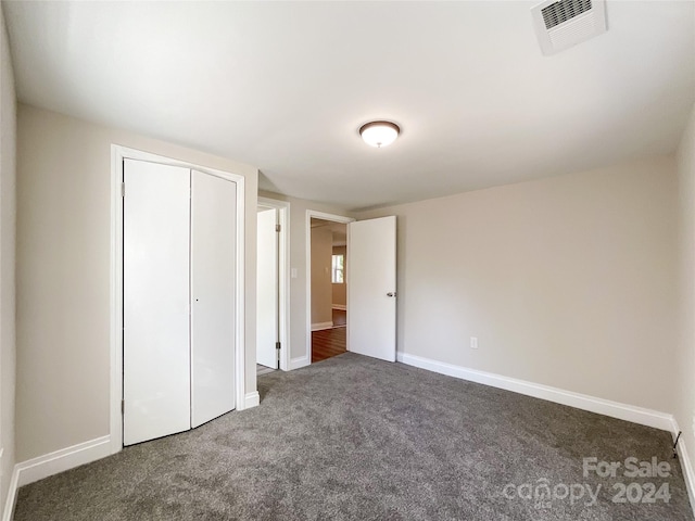 unfurnished bedroom featuring dark carpet and a closet