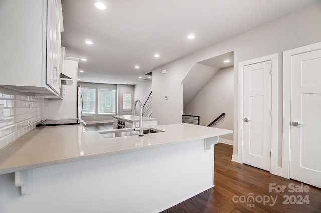 kitchen featuring white cabinets, sink, decorative backsplash, dark hardwood / wood-style flooring, and kitchen peninsula