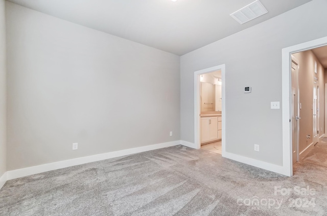 unfurnished bedroom featuring light carpet and ensuite bath