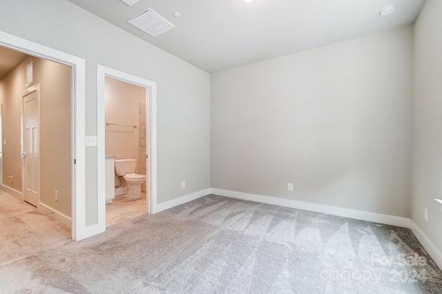 unfurnished bedroom with light colored carpet, a spacious closet, and ensuite bathroom