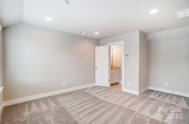 unfurnished bedroom featuring ensuite bath, light carpet, and lofted ceiling