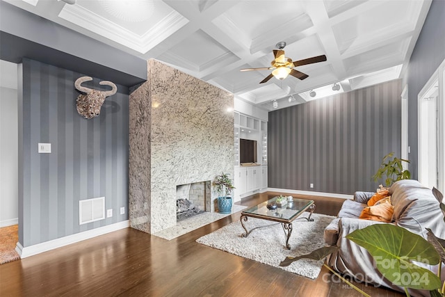 living room with dark hardwood / wood-style flooring, beamed ceiling, a stone fireplace, and coffered ceiling