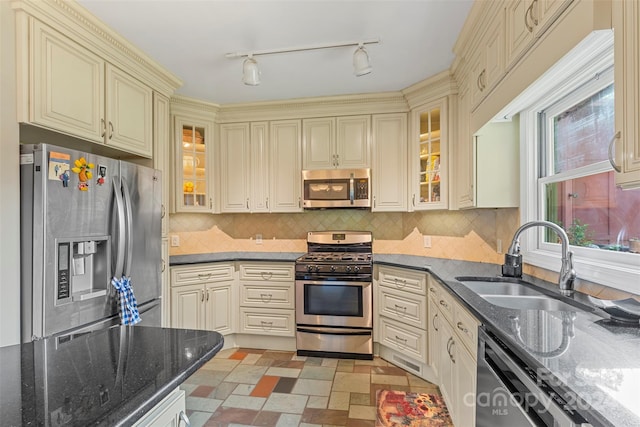 kitchen with dark stone countertops, decorative backsplash, sink, stainless steel appliances, and cream cabinetry