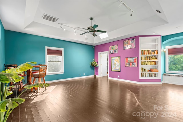 game room with rail lighting, a tray ceiling, built in features, and a healthy amount of sunlight