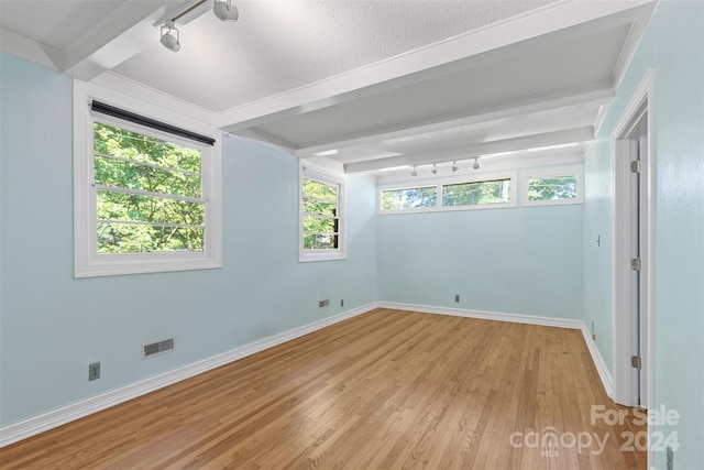 empty room featuring light hardwood / wood-style floors, a textured ceiling, and beam ceiling