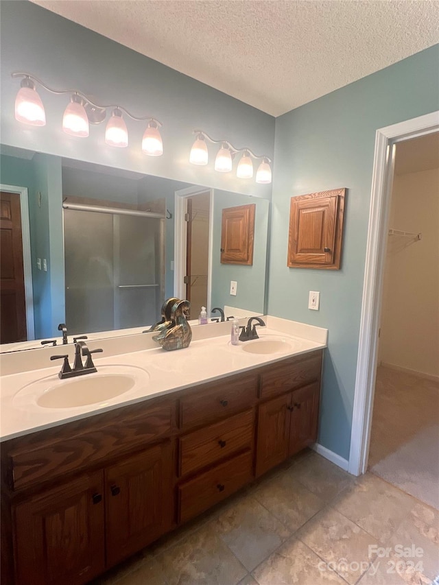 bathroom with a textured ceiling, tile patterned flooring, a shower with door, and vanity