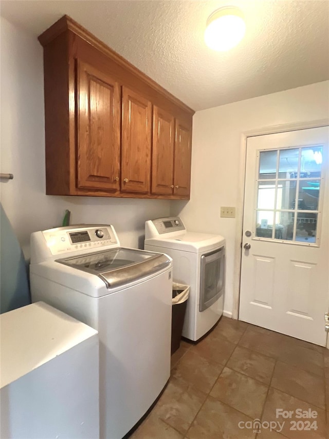 laundry area with washer and dryer, cabinets, a textured ceiling, and dark tile patterned floors