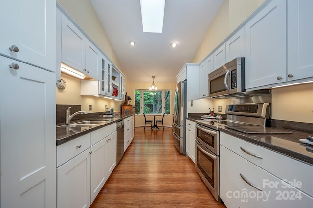 kitchen featuring lofted ceiling with skylight, sink, white cabinetry, decorative light fixtures, and appliances with stainless steel finishes