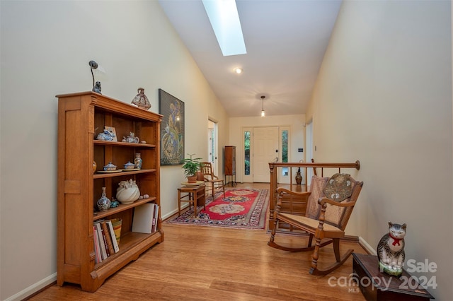 corridor featuring high vaulted ceiling, a skylight, and light hardwood / wood-style floors