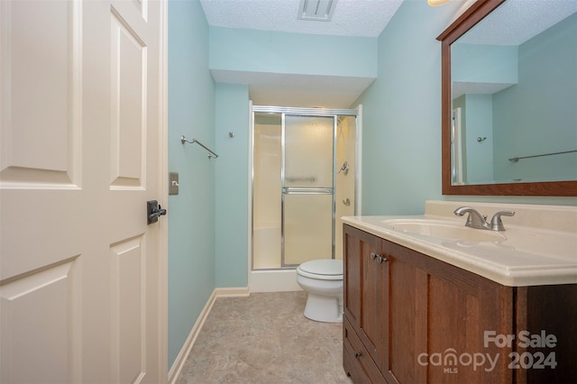 bathroom with vanity, toilet, a textured ceiling, and a shower with shower door