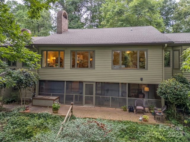 rear view of house with a patio area, a shingled roof, a chimney, and a sunroom