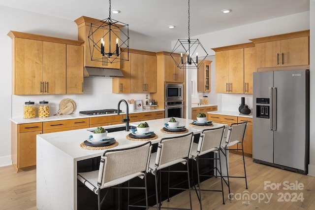 kitchen featuring decorative light fixtures, a kitchen island with sink, a chandelier, light hardwood / wood-style flooring, and stainless steel appliances