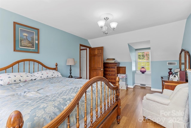 bedroom featuring wood-type flooring, vaulted ceiling, and an inviting chandelier