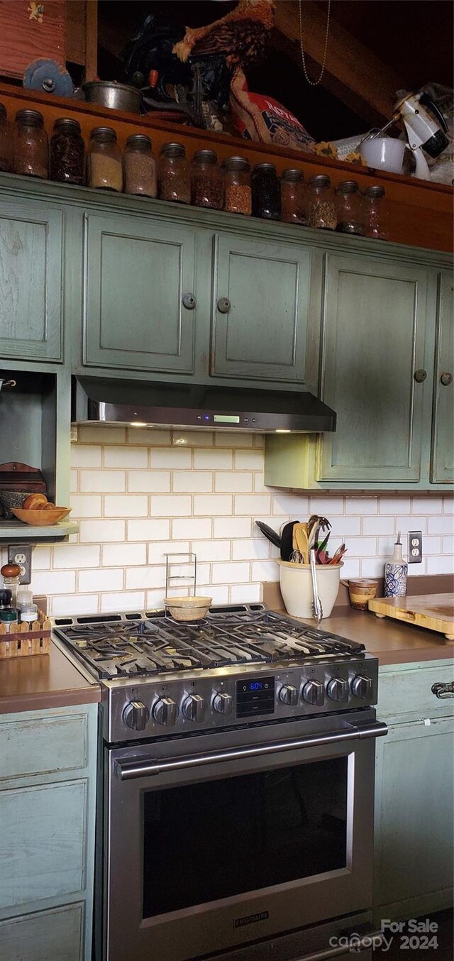 kitchen with green cabinets, high end range, and backsplash