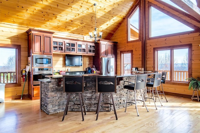 kitchen with a kitchen breakfast bar, stainless steel appliances, light wood-style floors, wooden walls, and wood ceiling