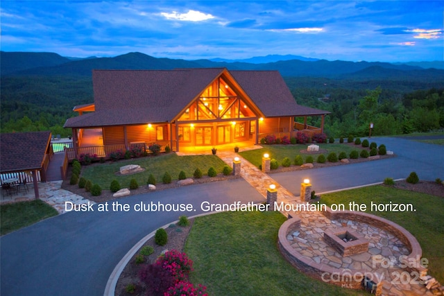 view of front facade featuring a mountain view, curved driveway, a lawn, and an outdoor fire pit