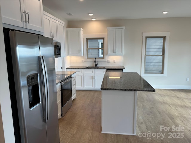 kitchen featuring a sink, tasteful backsplash, a center island, dark stone counters, and appliances with stainless steel finishes