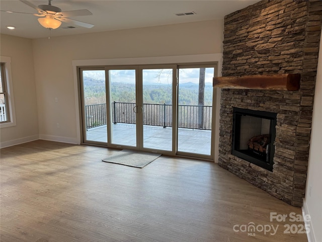 unfurnished living room with baseboards, visible vents, a fireplace, ceiling fan, and light wood-type flooring