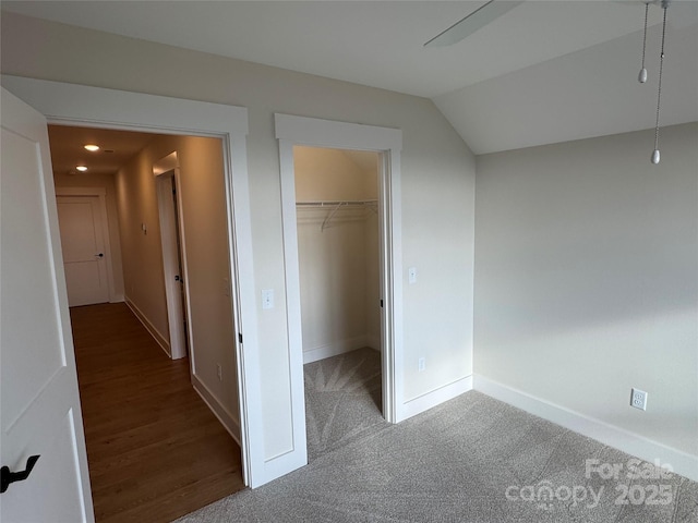 unfurnished bedroom featuring a walk in closet, lofted ceiling, baseboards, and a closet