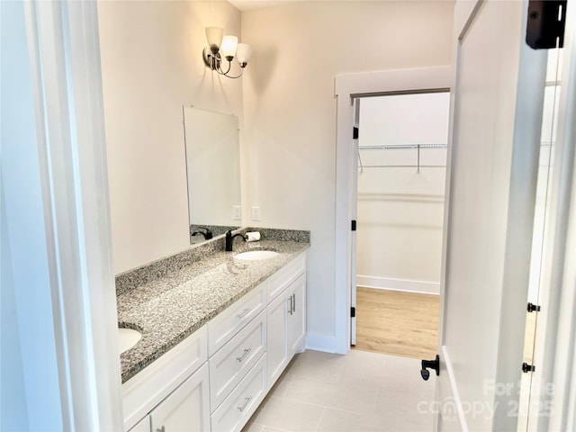 bathroom featuring tile patterned floors, a walk in closet, a sink, double vanity, and baseboards