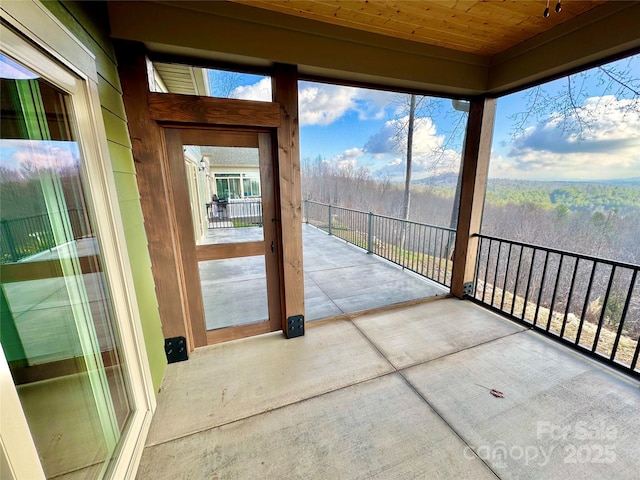 unfurnished sunroom featuring wood ceiling and a view of trees