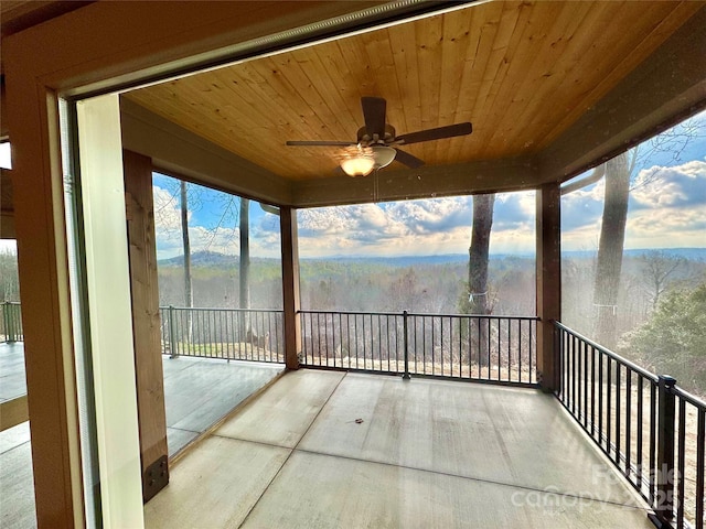 unfurnished sunroom featuring wooden ceiling, a ceiling fan, and a forest view