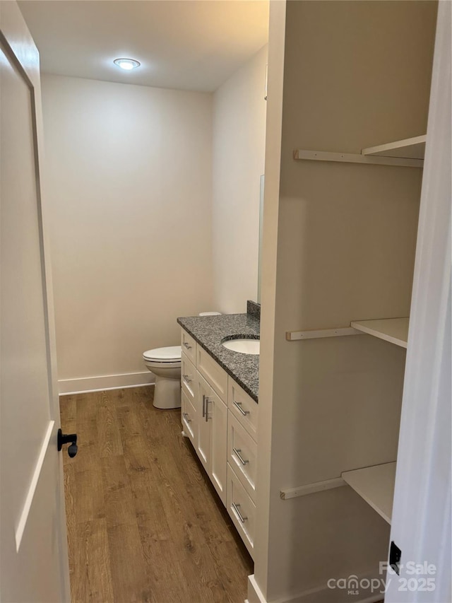 bathroom featuring baseboards, toilet, wood finished floors, and vanity