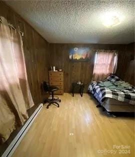 bedroom featuring a textured ceiling, light wood-type flooring, wooden walls, and baseboard heating