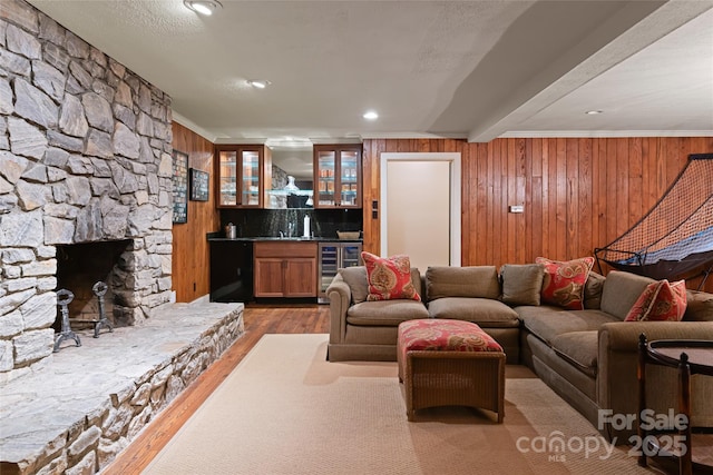 living room featuring wooden walls, a stone fireplace, wet bar, beverage cooler, and light wood-type flooring