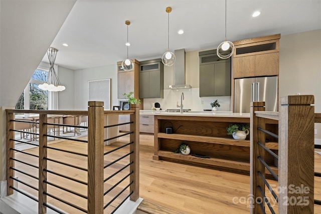 kitchen featuring pendant lighting, light wood-type flooring, high end fridge, and wall chimney exhaust hood