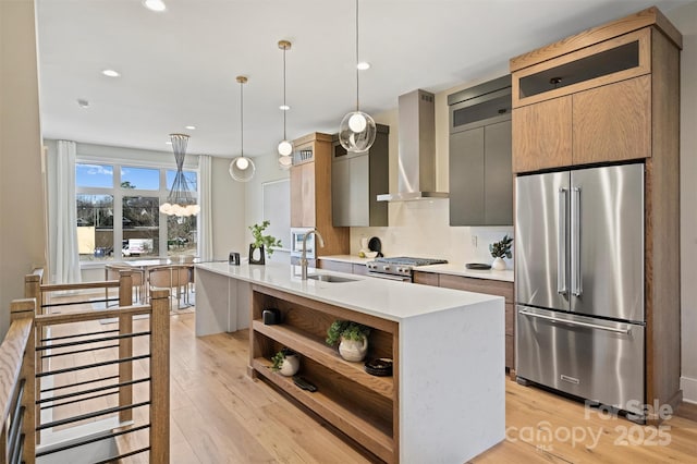 kitchen featuring sink, stainless steel appliances, wall chimney range hood, pendant lighting, and a center island with sink