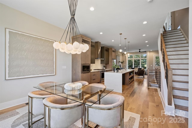 dining space with ceiling fan with notable chandelier, light wood-type flooring, and sink