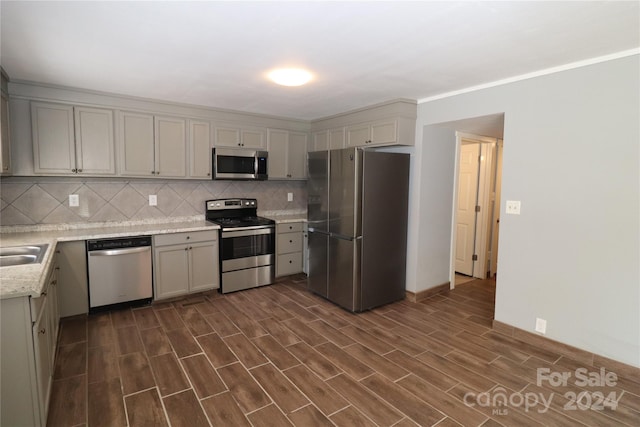 kitchen with gray cabinetry, backsplash, dark wood-type flooring, stainless steel appliances, and light stone counters