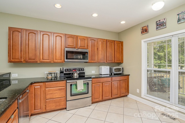 kitchen featuring light tile patterned floors, stainless steel appliances, and dark stone counters