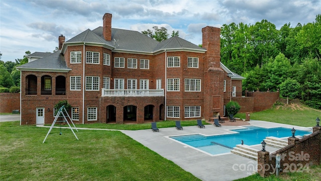 rear view of house featuring a balcony, a lawn, and a patio