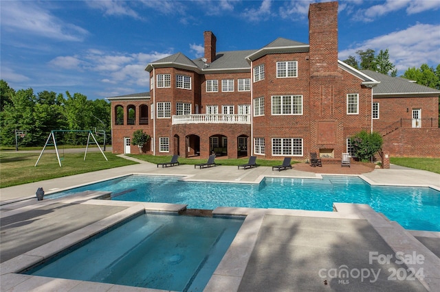 rear view of property featuring a playground, a lawn, a swimming pool with hot tub, an outdoor fireplace, and a patio