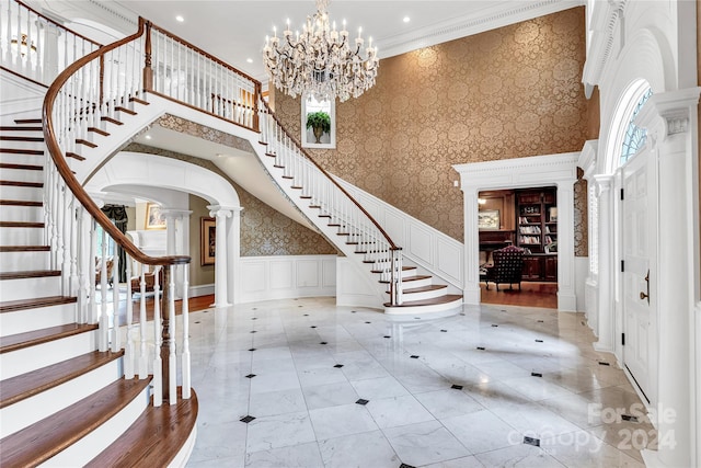 entrance foyer featuring crown molding, a notable chandelier, a high ceiling, and ornate columns